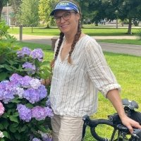 woman standing next to flowers holding onto her bicycle