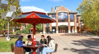 Four Saint Lawrence students sit at a scarlet dolar charging table outside of the Sullivan Student Center.