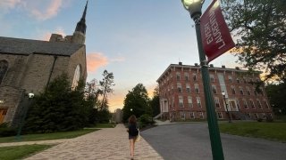 A student walks up a path between a stone church and an academic building on the Saint Lawrence University campus at sunet.
