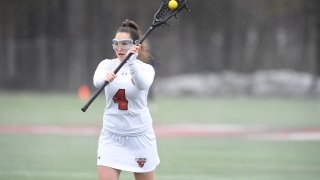 Nicole Stanton, wearing a white Saint Lawrence University lacrosse uniform, cradles the ball and prepares to pass during a home game. 