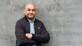 Dr. Somdeep Sen '07 stands with his arms crossed next to a concrete wall.