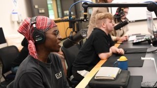 A student wearing a checkered headscarf speaks into a microphone in the University's podcasting studio.