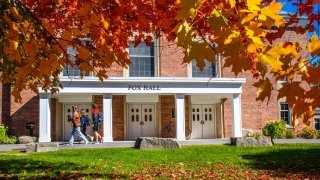 A group of students walk by Fox Hall on a beautiful fall day. Vibrant orange, red, and yellow leaves are in the close up.