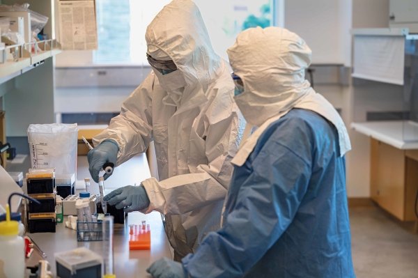 A student and faculty member wear protective equipment while working with lab equipment.