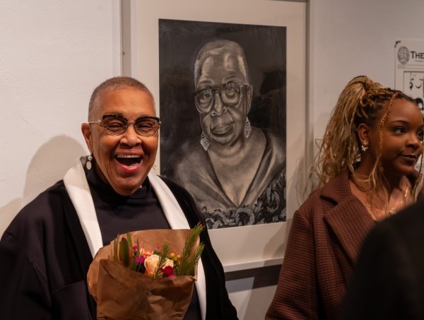 Margaret Bass smiles big next to her black and white portrait. Artist Nadirah Croft stands next to the portrait.