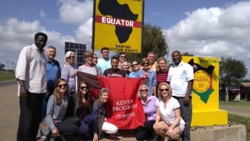 Group of Alumni on trip to Kenya in 2019 pictured in front of the equator crossing signs.