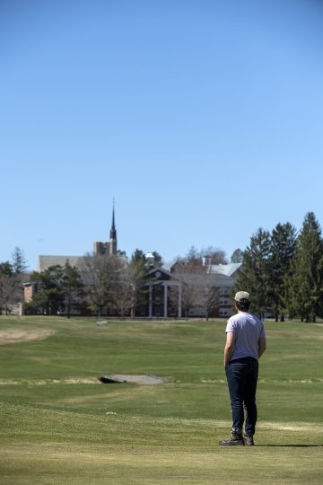 Man standing looking out over a field toward a chapel in the distance