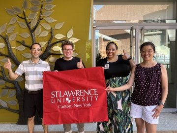 Photo of Grace Huang abroad with Saint LAwrence University ALumni holding a Saint Lawrence University Flag.