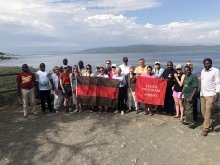 A photo of St Lawrence students and partners in Kenya standing in front of a picturesque lake holding St Lawrence flags.
