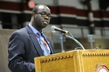 A photo of Okoth standing behind a podium. 