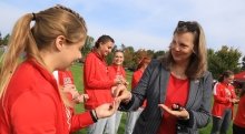 President Morris hands lady bug bracelets to smiling members of the Saints Women's Cross Country Team.