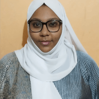 Nafisa smiles while wearing a black glasses, a white headscarf, and a black and white stripped dress.