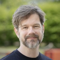 A guy with a graying beard tries to look kind and thoughtful while being photographed.