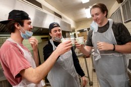 Three students cheers their cups of hot chocolate in a ktichen.
