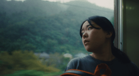 Film still from Chronicle of a City showing a woman looking out a train window.