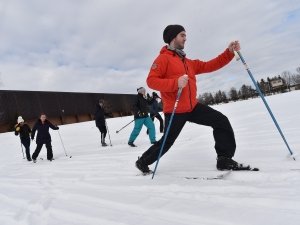 A student glides across the snow on cross-country skis. In the background, others are learning how to ski.