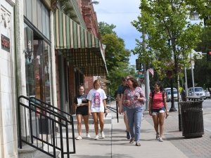 Four students and a professor walk on a main street, lined with shops, on a sunny day in Canton, New York.