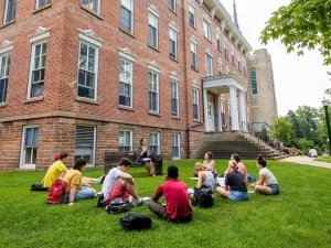 A professor sits on a bench outside of Richardson Hall, delivering a lecture to a group of students seated around her. It's a warm late summer day, perfect for an outdoor class.