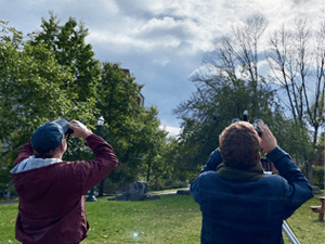 Two people use binoculars and peer up to the sky during a partial eclipse.