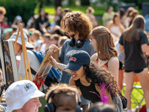 Students gather outdoors, painting and enjoying a campus event in the sun.