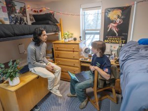 Two students talk inside a Saint Lawrence University dorm room with lofted beds, desks, plants, and string lights decorating the space.