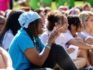 A group of students sitting outside on a sunny day, smiling and clapping during an event at Saint Lawrence University.