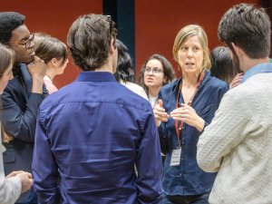 A group of people stands in a circle having a conversation, with one person speaking and gesturing while others listen attentively.