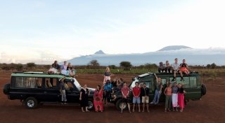 Several Saint Lawrence students stand in front of two safari vehicles in Kenya. Mountains are in the distance.