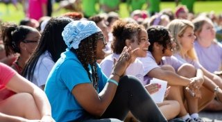 A group of students sitting outside on a sunny day, smiling and clapping during an event at Saint Lawrence University.