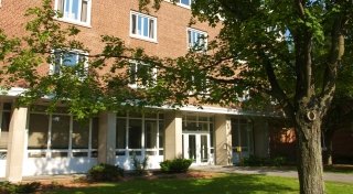 Exterior of Whitman Hall, a four-story red-brick building with large windows and a glass entryway, surrounded by trees and grass.