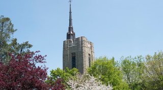The stone tower and copper spire of Gunnison Memorial Chapel visible over trees in bloom for spring.