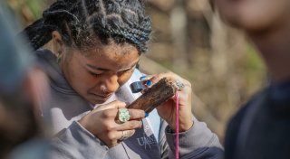 A student examines a piece of bark with a magnifying glass. 