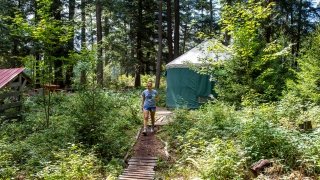 Person walking through the wood sin front of a yurt