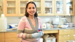 Professor Ana Estevez, wearing surgical globes, holds a test tube while standing in her lab. 