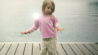 Brynn Afton as a small child around the age of three standing on a dock overlooking Saranac Lake.