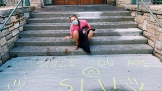 Chloe Mitchell smiles next to sidewalk-chalk writing that says "smile, you are at SLU."