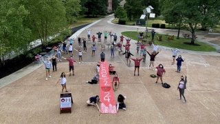 A large group of socially-distanced students stand outside holding a "Class of 2024" sign.