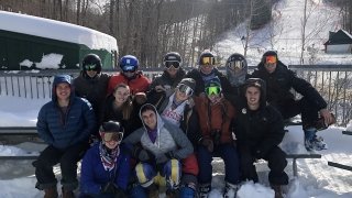 A group of Saint Lawrence club ski students sit on a snow covered bench at a ski mountain. 