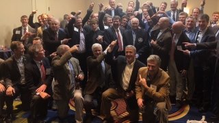 Coach Leet surrounded by former players enthusiastically celebrating him.