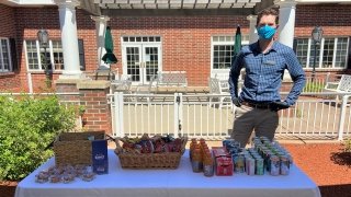 Conor McDermott, wearing a mask, stands behind a table with drinks and snacks on it.