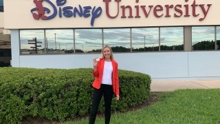 A student in professional attire stands in front of a corporate building with the "Disney University" logo on it.