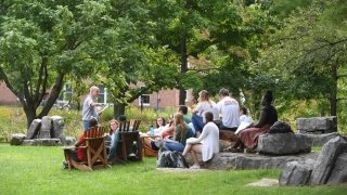 A professor delivers a lecture to students seated on rocks and Adirondack chairs outside on the Saint Lawrence University campus.