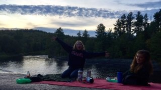 Two students sitting on a blanket on the rocks at the top of a waterfall at dusk. 