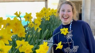 Grace Harkins with a wide smile stands among a garden of daffodils.