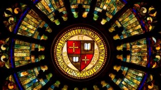 A decorative and elaborate stained-glass window with the Saint Lawrence University motto and shield at its center.