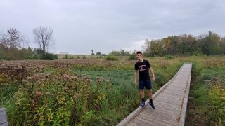 A student stands on a plank bridge over a gravel trail in a field of wildflowers.