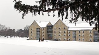 A modern stone residence hall on a gray day in winter. Snow covers the ground on the quad in front.
