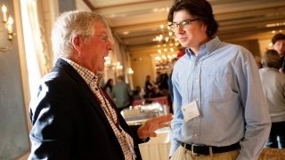 A young man in professional attire talks to his alumni mentor, an older man also in professional attire.