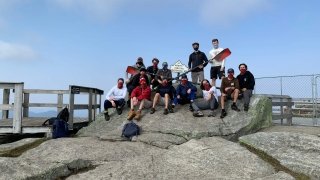 Twelve member of the Saint Lawrence Men's Rowing team at the peak of Whiteface Mountain, holding two rowing oars.