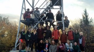 A large group of students gather for a photo at the base of a fire tower atop Mount Azure. 